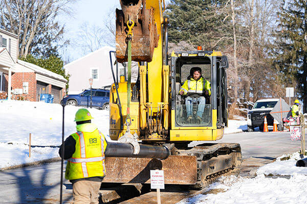 Lowering a stick of ductile iron water main pipe into the trench