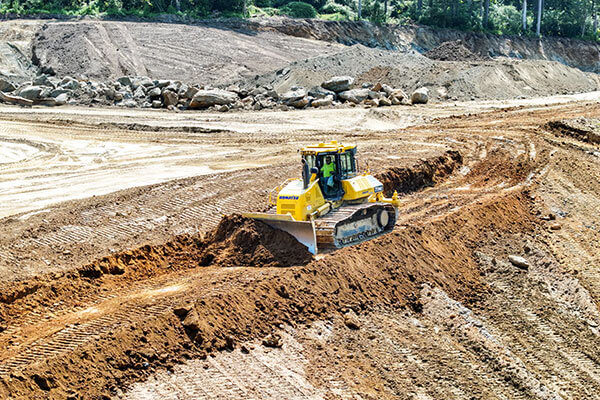A bright yellow bulldozer pushes earth on a large construction site, with mounds of dirt and rocks in the background, conveying a sense of industrious activity.
