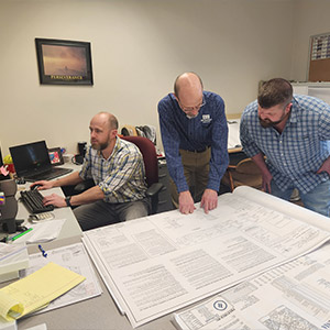 Brubacher team surrounding desk full of blueprints.